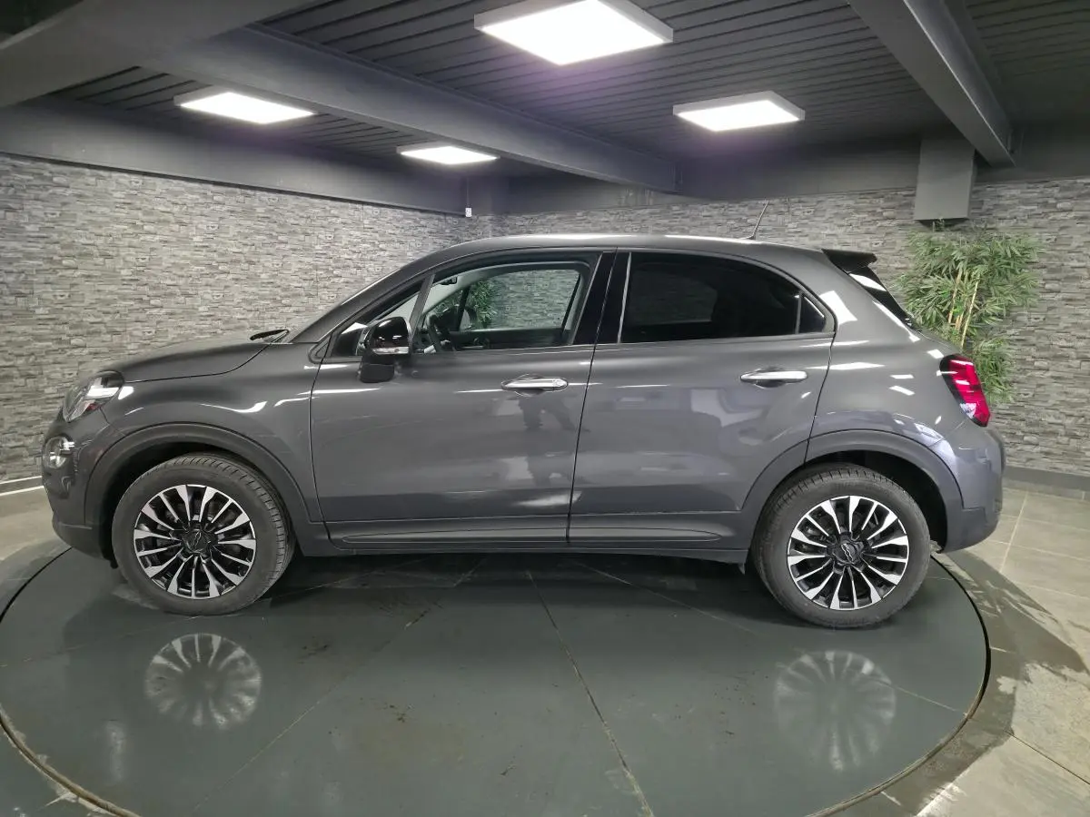 Vue de profil côté gauche d'un Fiat 500X gris avec jantes alliage 17 pouces dans un showroom intérieur.