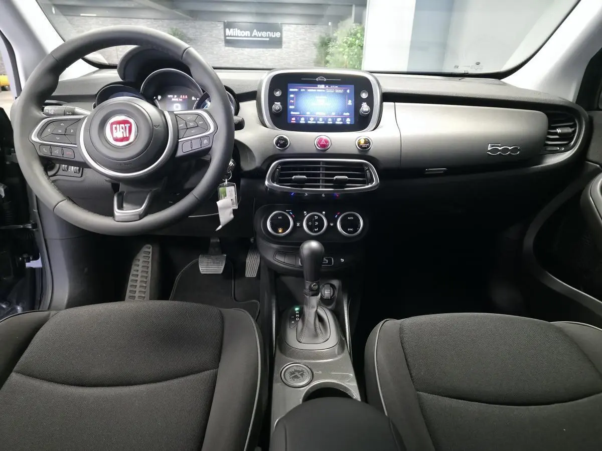 Vue intérieure avant du tableau de bord gris titane et volant noir du Fiat 500X 2024 avec écran tactile central et levier de boîte automatique.