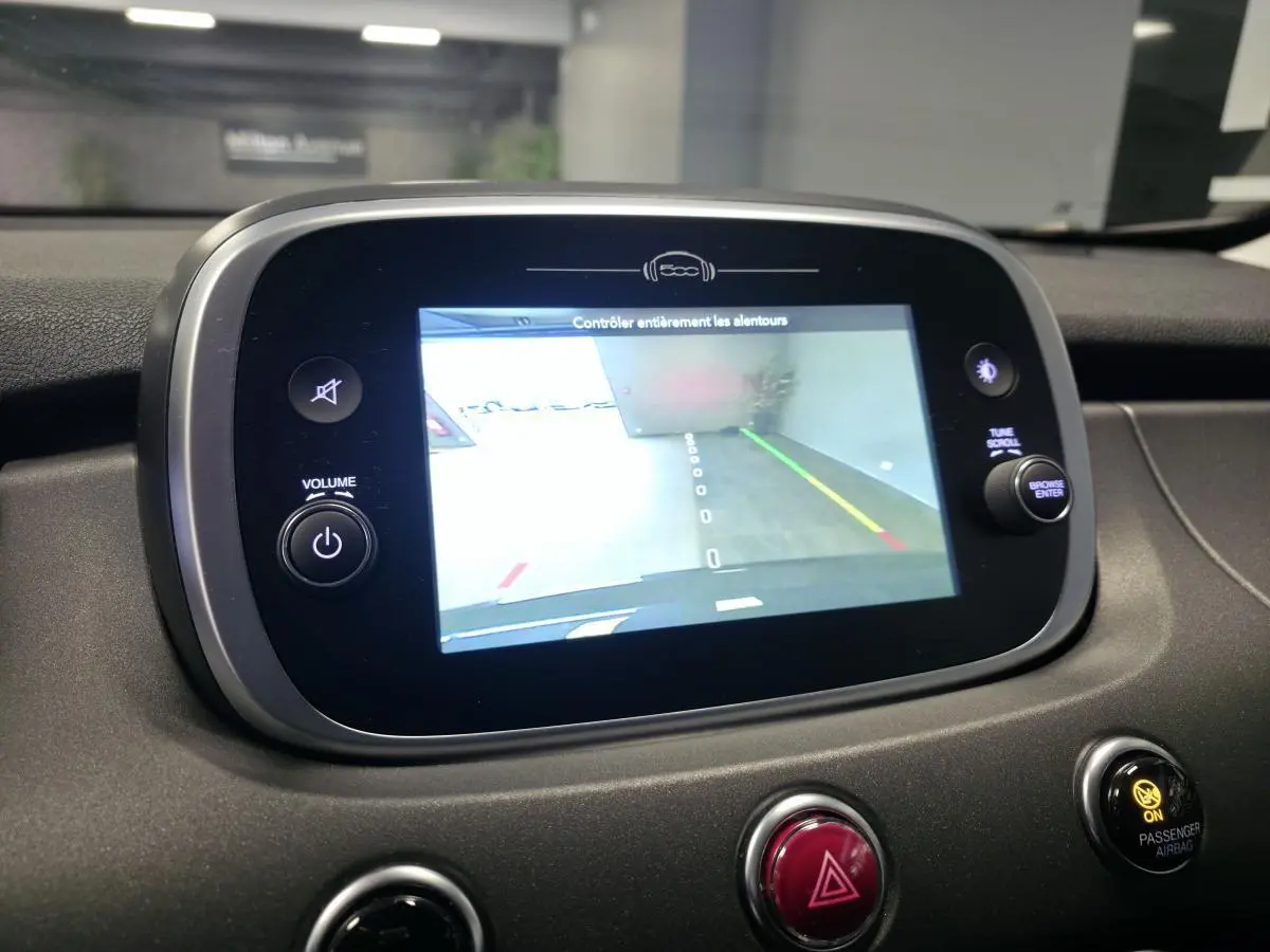 Écran central tactile de la Fiat 500X 2024 montrant la caméra de recul, avec tableau de bord gris et commandes autour.