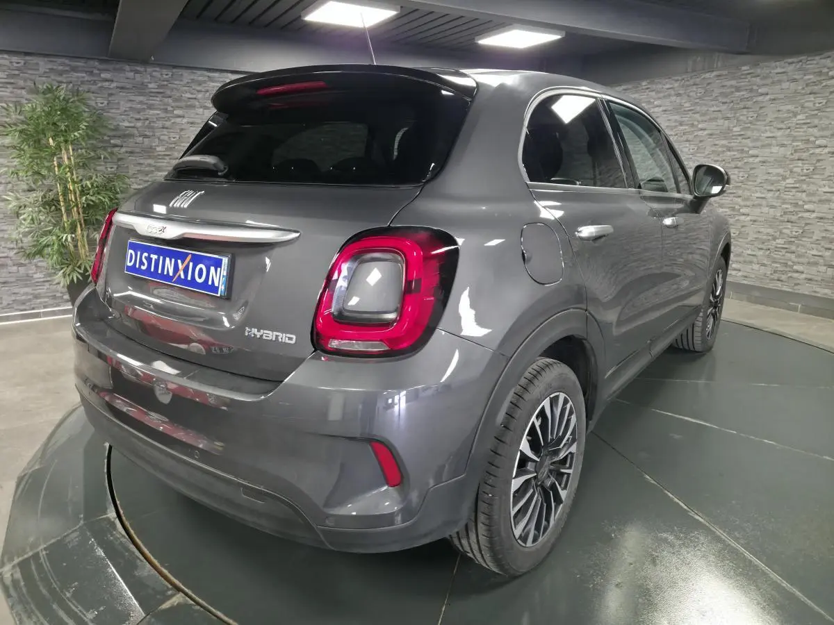 Vue 3/4 arrière droite d'une Fiat 500X gris avec feux arrière LED et jantes alliage 17 pouces dans un showroom.