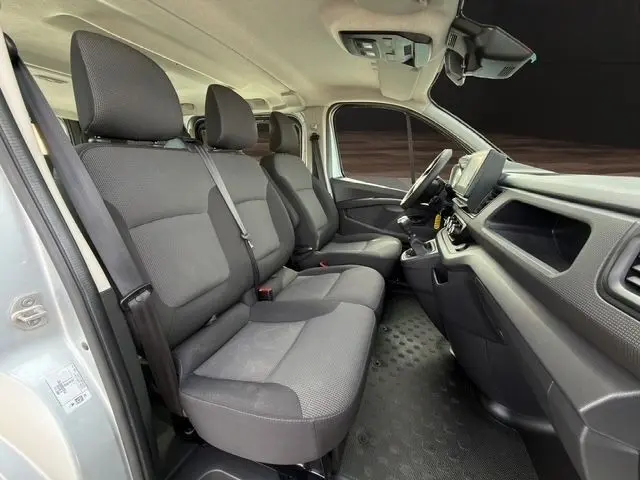 Vue intérieure côté conducteur du Renault Trafic Fourgon gris clair 2022, montrant les sièges avant et la planche de bord moderne.
