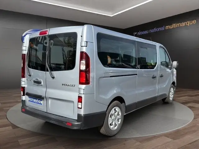Vue 3/4 arrière droite d'un Renault Trafic Fourgon gris clair, avec vitres latérales teintées et feux arrière verticaux.