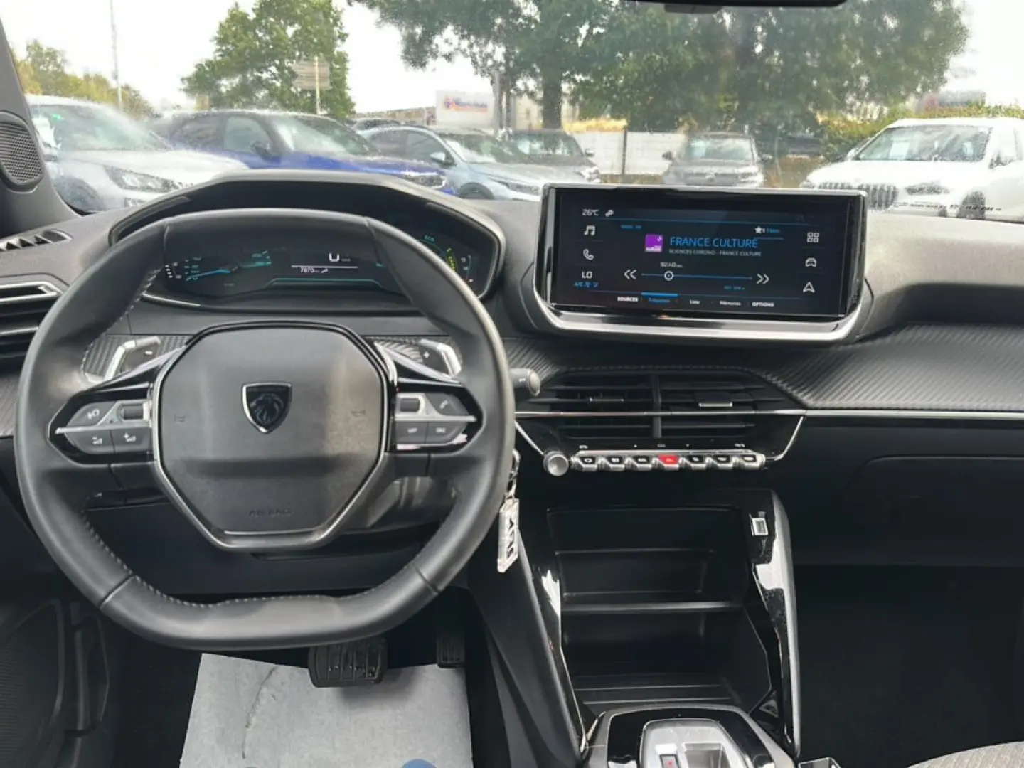 Vue intérieure avant centrée sur le volant et l'écran tactile du tableau de bord du Peugeot 2008 gris 2025.