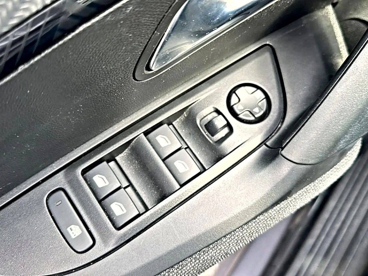 Gros plan sur les commandes de lève-vitres et réglage des rétroviseurs côté conducteur d’un Peugeot 2008 gris.