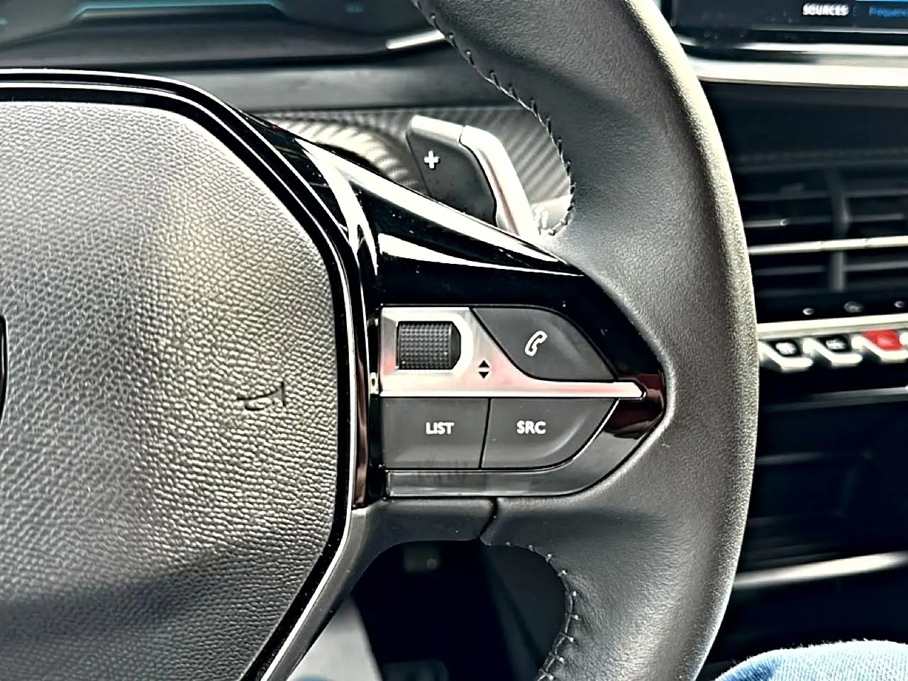 Gros plan sur le volant noir de la Peugeot 2008 1.2 hybrid 145 style, avec commandes multifonctions visibles.