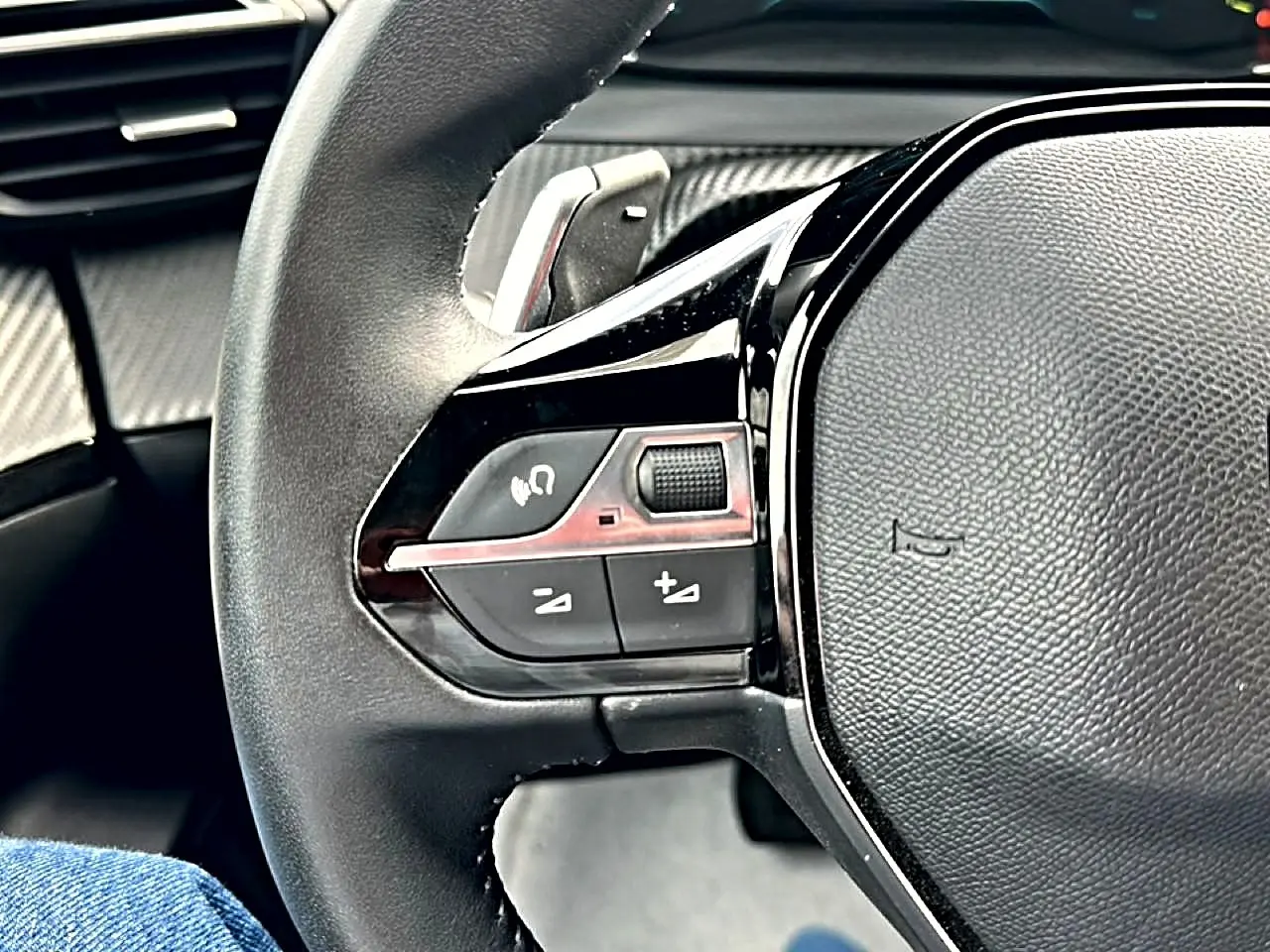 Gros plan sur le volant noir multifonction du Peugeot 2008 1.2 hybrid 145 style, avec commandes intégrées côté gauche.
