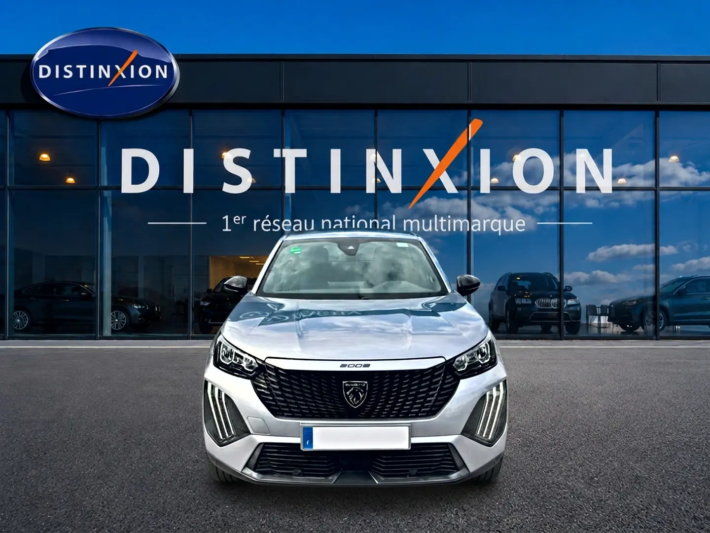 Vue frontale d'un Peugeot 2008 gris 2025 avec calandre noire et feux LED verticaux, devant une vitrine Distinxion.