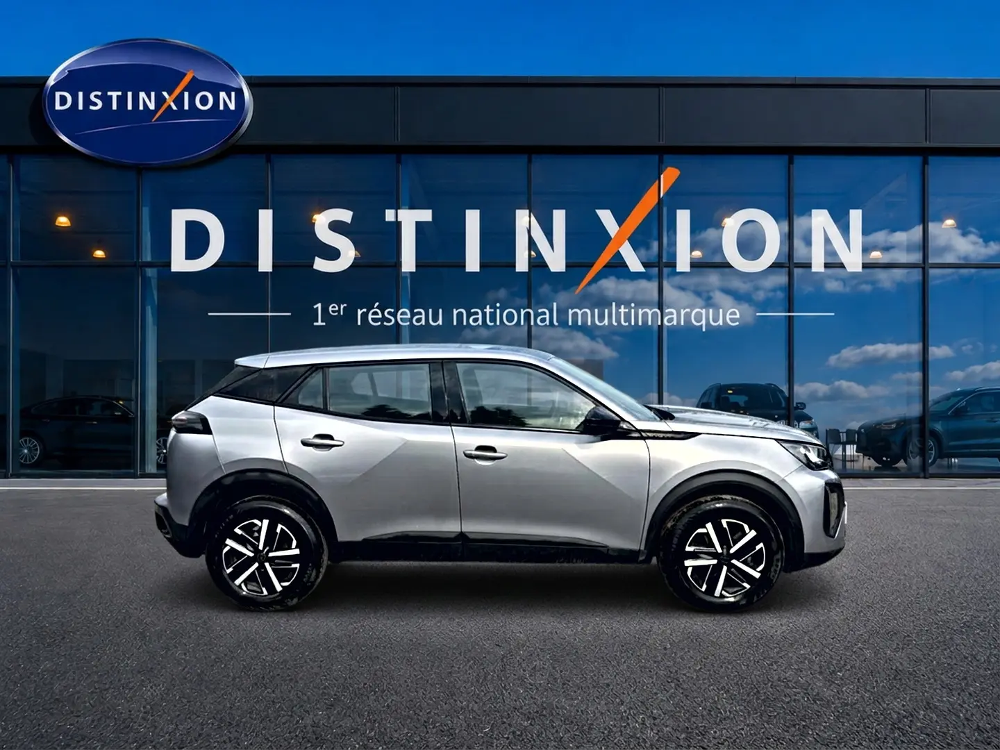 Peugeot 2008 gris en profil droit, avec jantes noires et toit noir, devant une vitrine Distinxion.