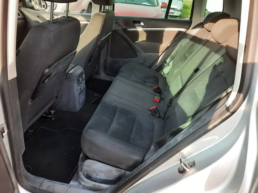 Vue intérieure arrière côté droit du Volkswagen Tiguan gris argent 2012, sièges arrière en tissu noir avec ceintures visibles.