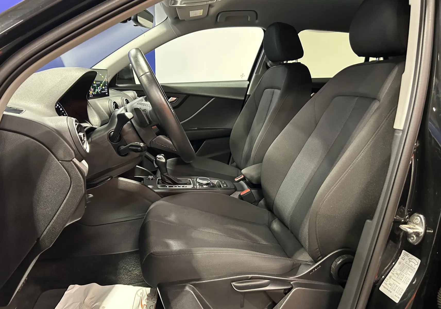 Intérieur noir de l'Audi Q2 35 TFSI 2023 vu côté conducteur, avec sièges tissu et tableau de bord moderne.