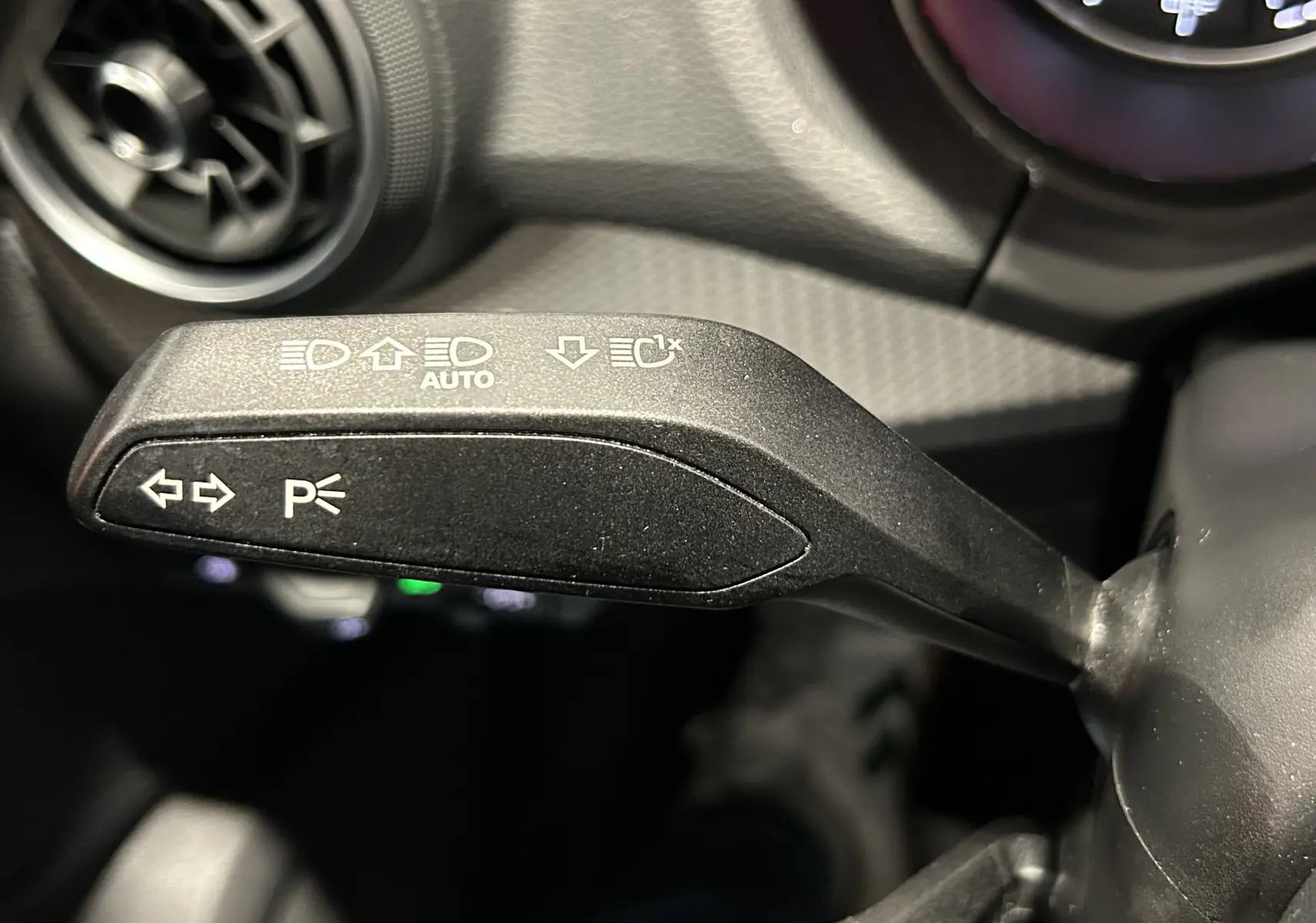 Gros plan sur le bouton de commande des phares avec réglage automatique, sur l'Audi Q2 noir métal 2023.