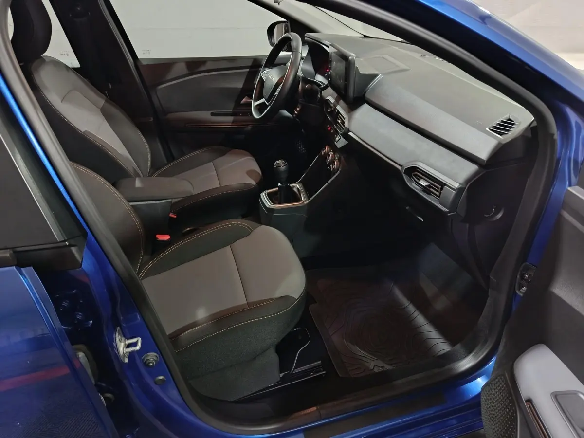 Vue intérieure côté conducteur d'une Dacia Sandero Extreme+ bleu 2024, montrant sièges, volant cuir et tableau de bord tactile.