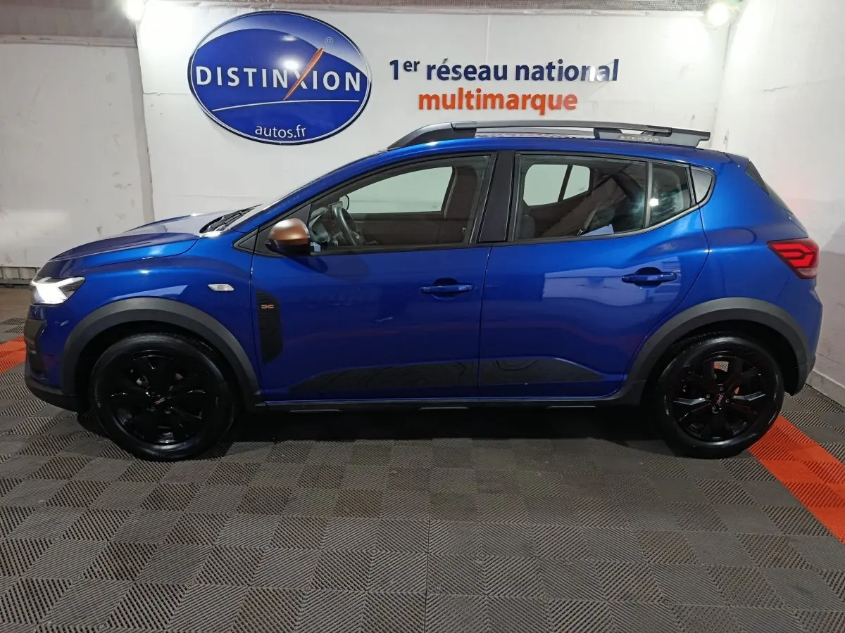 Vue latérale gauche d'une Dacia Sandero Extreme+ TCe 110 bleu 2024 avec jantes noires et rétroviseurs cuivrés.