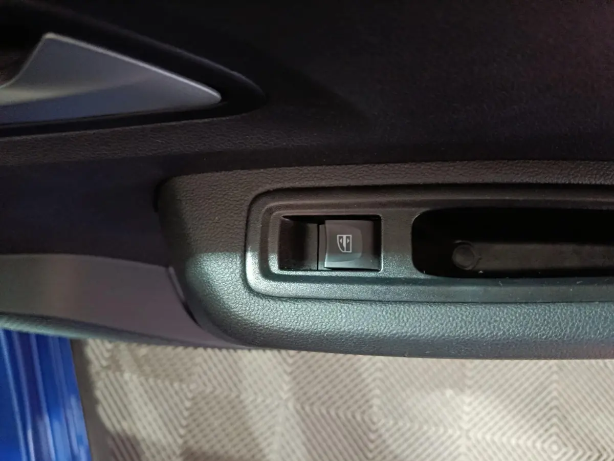 Gros plan sur le bouton de commande de la vitre électrique côté conducteur, avec partie de la porte bleu visible.