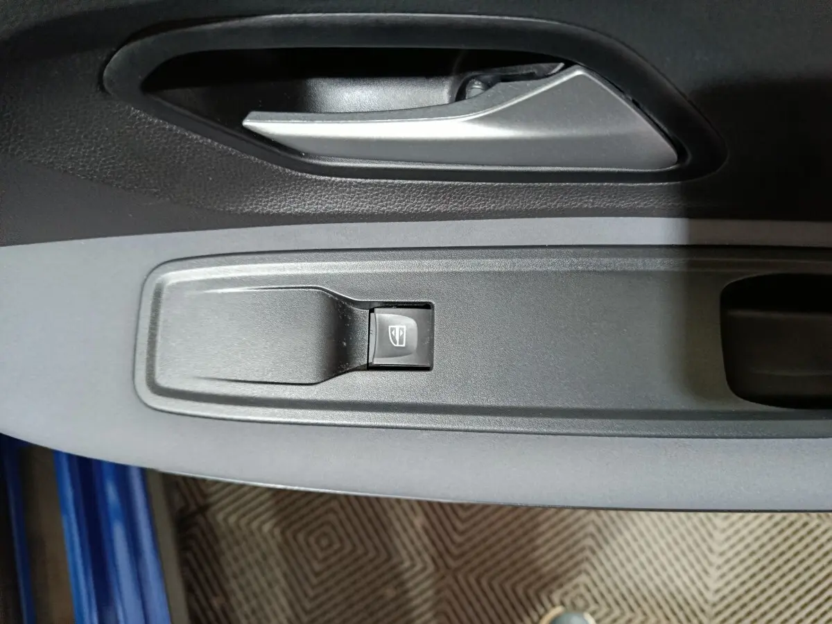 Détail de la commande de lève-vitre côté conducteur sur porte intérieure grise d'une Dacia Sandero bleu 2024.