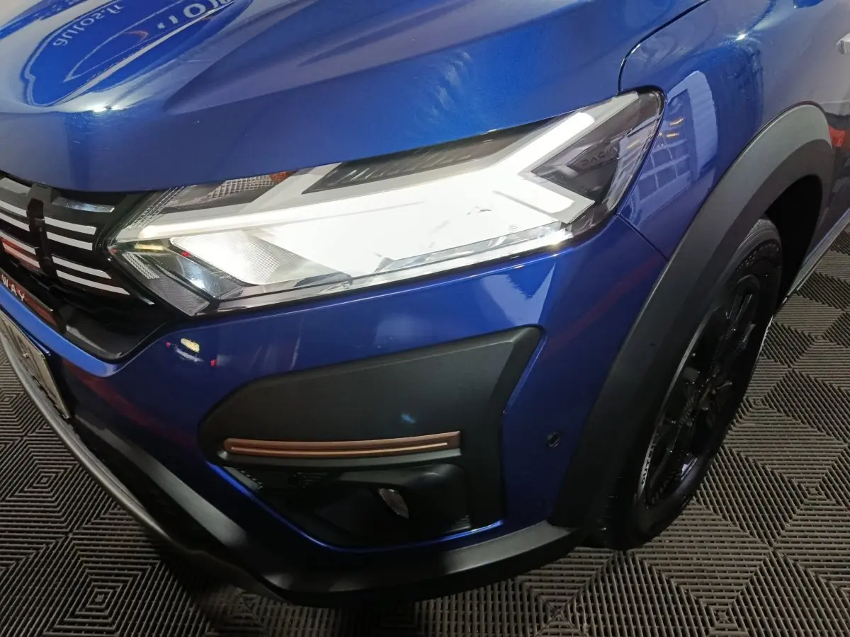 Gros plan sur l'avant droit bleu de la Dacia Sandero Extreme+ 2024, mettant en valeur le phare LED et la calandre noire.