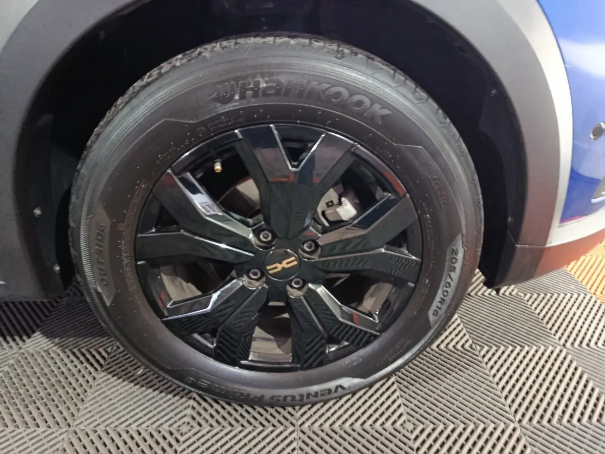 Gros plan sur la roue avant droite noire brillante d'une Dacia Sandero Extreme+ bleu 2024, jante alu distinctive.