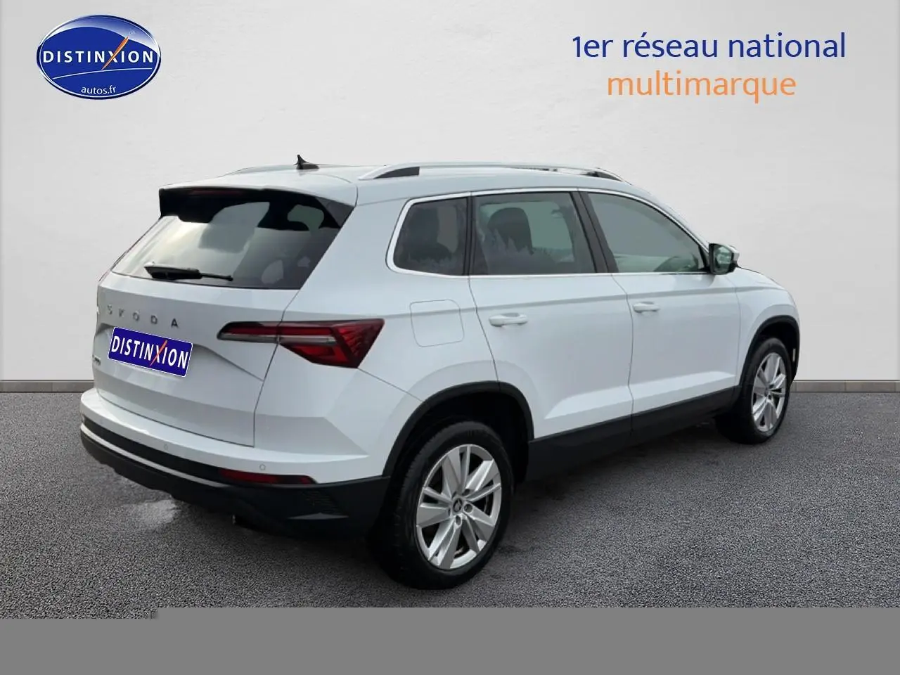Vue 3/4 arrière droite d'un Skoda Karoq blanc glacial avec barres de toit et jantes alu.