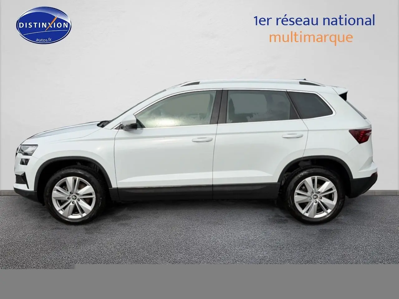 Vue latérale droite d'un Skoda Karoq blanc glacial avec jantes alu et barres de toit visibles.