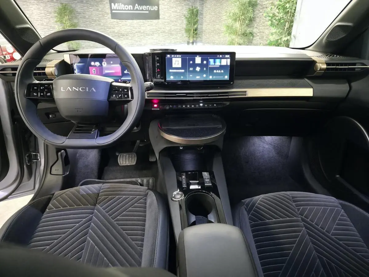 Vue intérieure avant de la Lancia Ypsilon 2025, avec tableau de bord digital et sellerie velours gris anthracite.