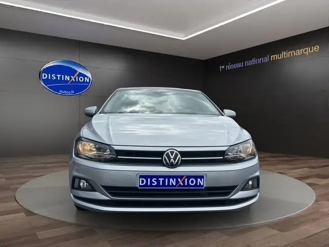 Vue de face d'une Volkswagen Polo gris clair 1.0 TSI 95 Lounge Business avec phares allumés en showroom