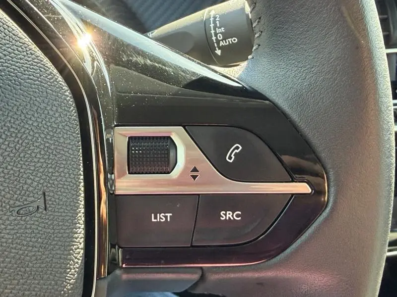 Gros plan sur les commandes audio et téléphone au volant d’une Peugeot 208 blanche, finition Allure 2025.