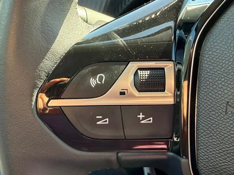 Gros plan sur les commandes audio et volume au volant noir du Peugeot 208 blanc Okénite, version Allure 2025.