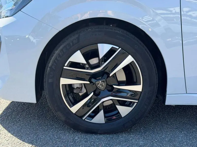 Gros plan sur la roue avant gauche d'une Peugeot 208 blanche, jante alliage noire et argentée avec logo Peugeot central.