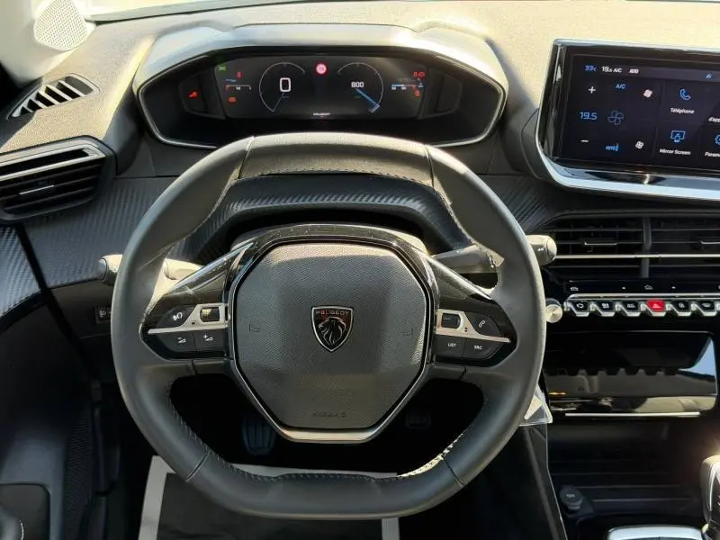 Vue intérieure centrée sur le volant multifonction noir de la Peugeot 208 1.2 100ch Allure avec tableau de bord digital et écran tactile.