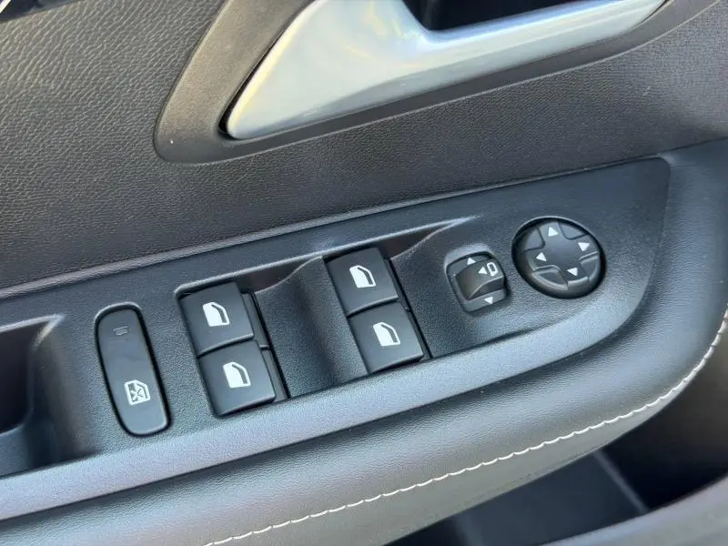 Gros plan sur les commandes des vitres et rétroviseurs côté conducteur de la Peugeot 208 blanche, avec surpiqûres blanches.