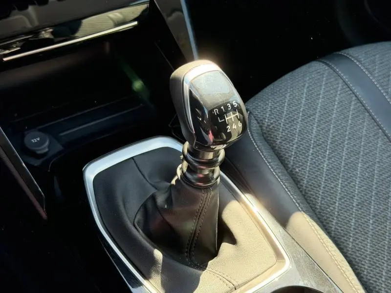Gros plan sur le levier de vitesses manuel noir et chrome de la Peugeot 208 1.2 essence, avec siège tissu gris à côté.