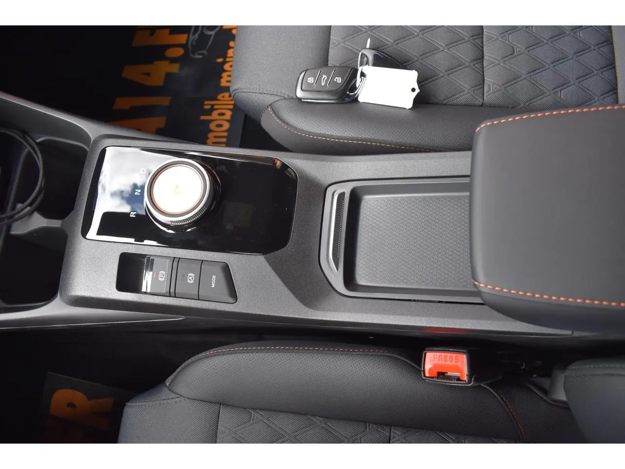 Vue plongeante sur la console centrale noire et les sièges noirs avec surpiqûres orange du MG3 Hybrid+ 2026, clé posée sur le siège.