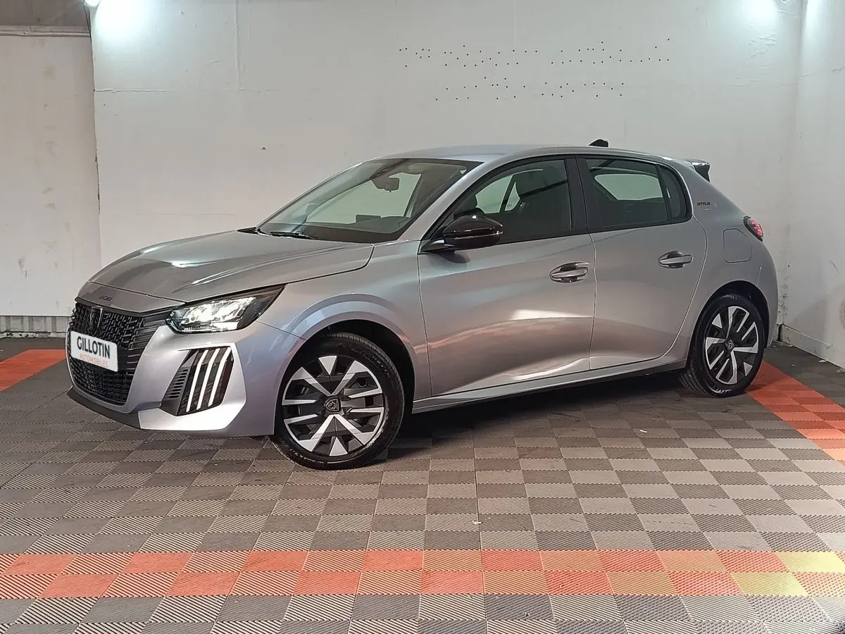 Peugeot 208 Hybrid gris clair vue de profil droit en intérieur, avec jantes stylisées et phares LED allumés.