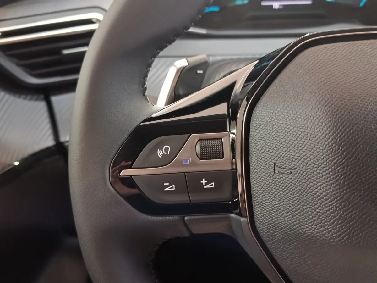 Gros plan sur le volant cuir multifonctions de la Peugeot 208 Hybrid 100 e-DCS6 Style, avec commandes audio intégrées.