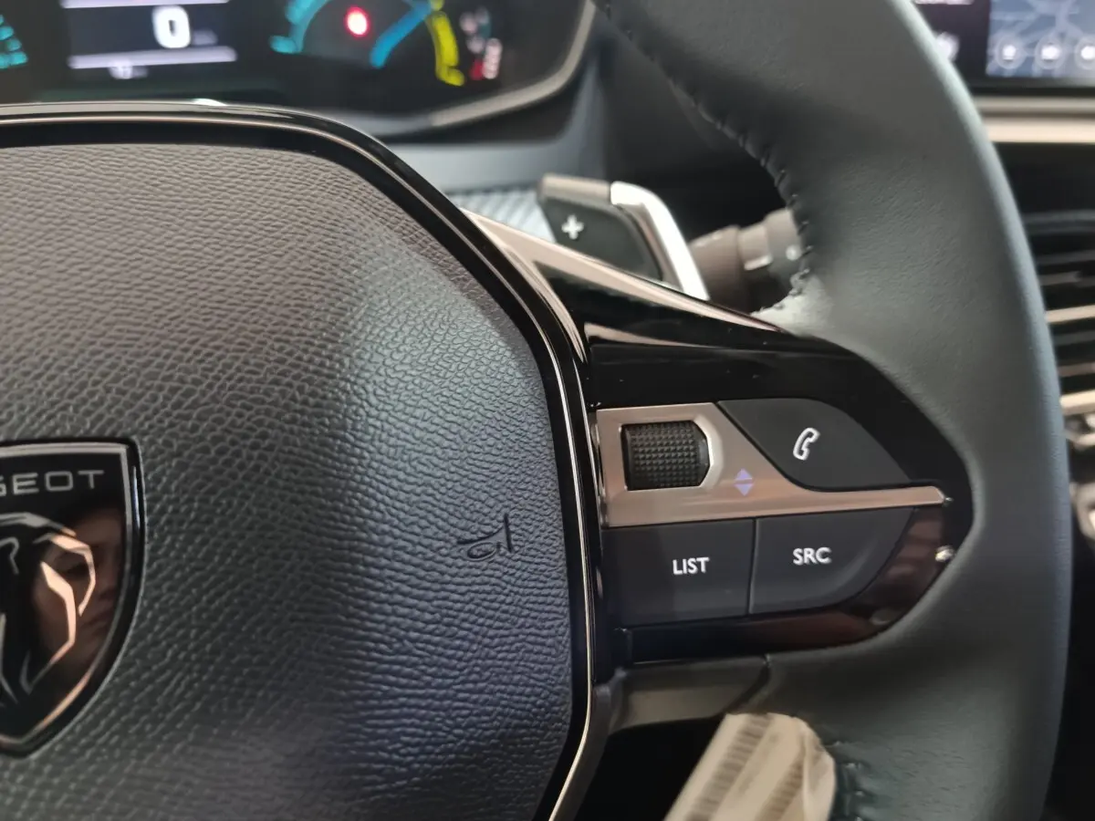 Gros plan sur le volant cuir noir de la Peugeot 208 Hybrid 100 e-DCS6 Style, avec commandes multifonctions visibles.