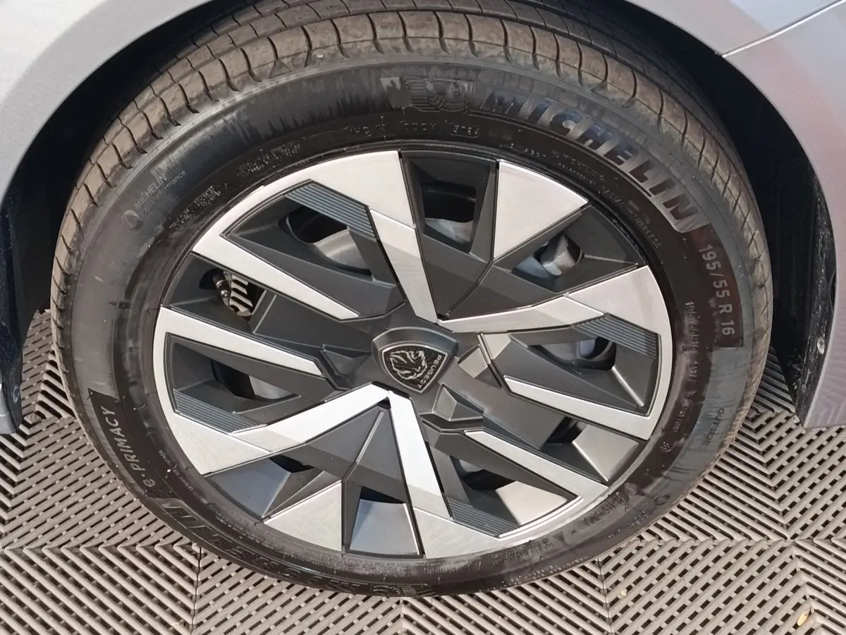 Gros plan sur la roue avant droite gris clair d’une Peugeot 208 Hybrid avec jante au design géométrique noir et argent.