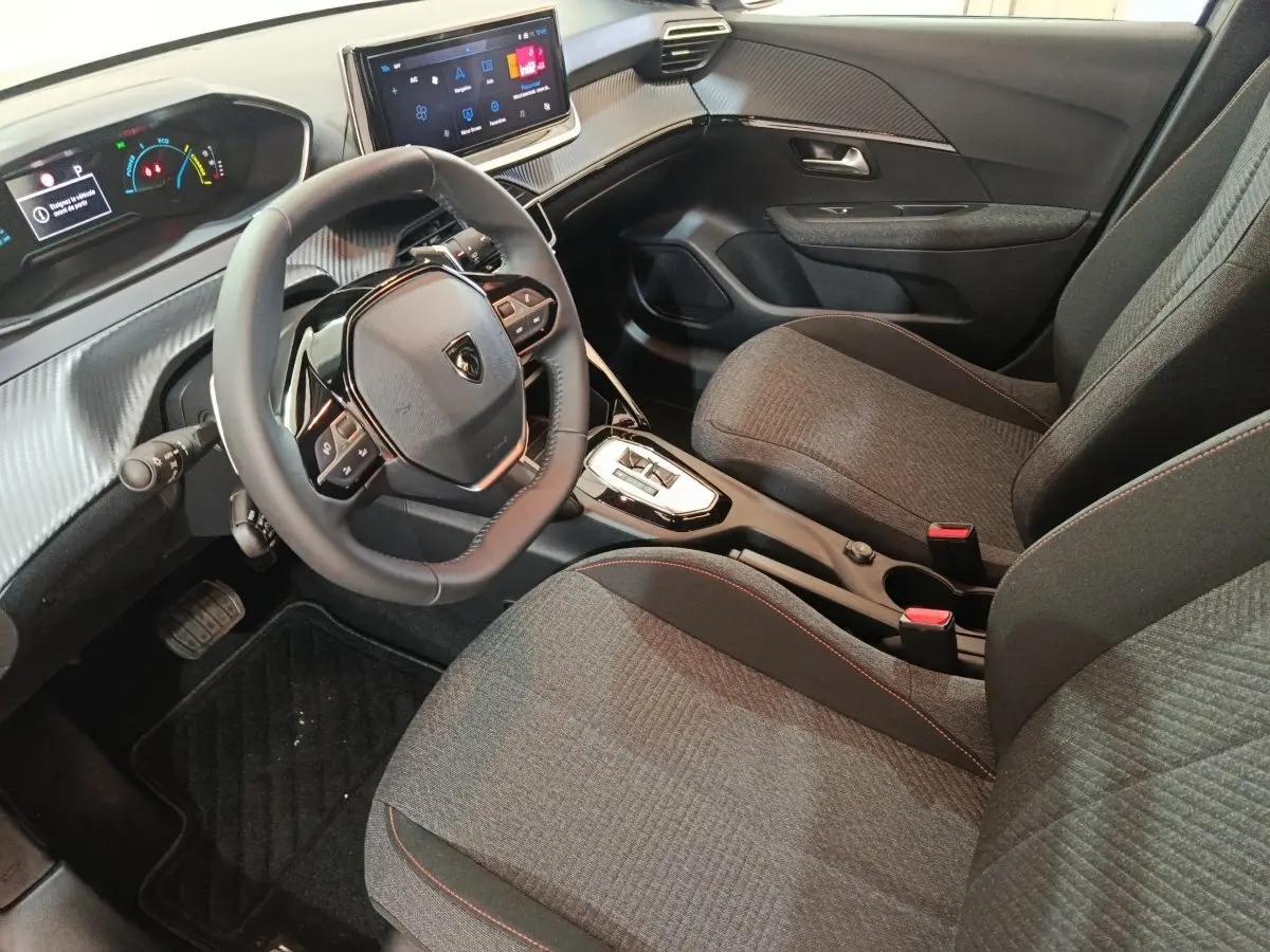 Vue intérieure côté conducteur de la Peugeot 208 Hybrid 100 e-DCS6 Style 2025, sièges gris et volant cuir multifonctions.
