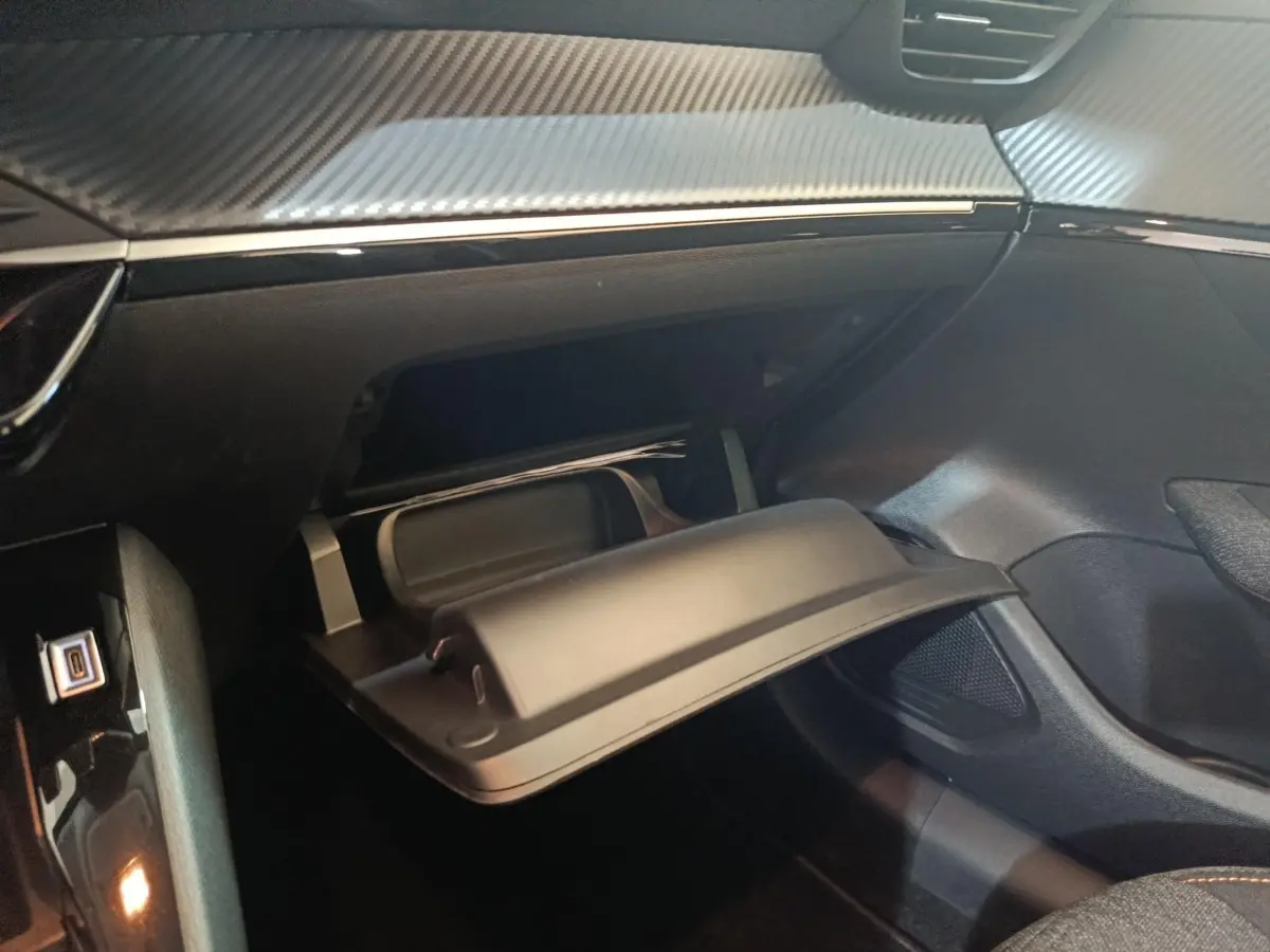 Gros plan sur la boîte à gants ouverte de la Peugeot 208 Hybrid gris clair, montrant le tableau de bord et les finitions intérieures.