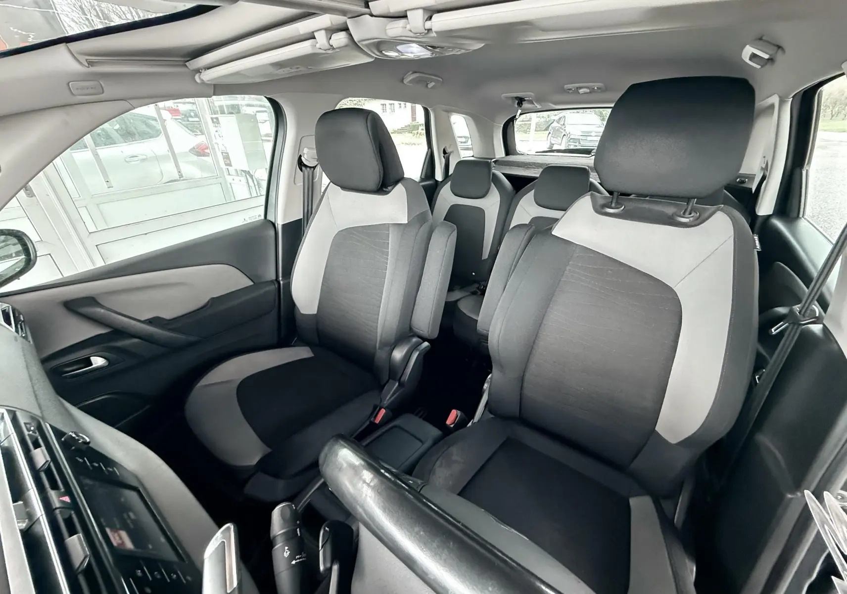 Vue intérieure avant droite du Citroën C4 Picasso 2015 avec sièges tissu noir et gris clair, toit ouvrant panoramique visible.