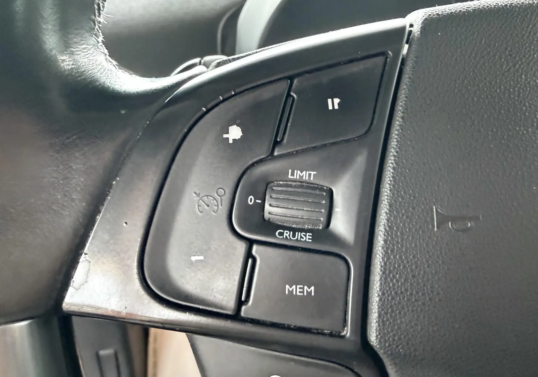 Gros plan sur les commandes de régulateur de vitesse au volant noir d'une Citroën C4 Picasso gris platinium.