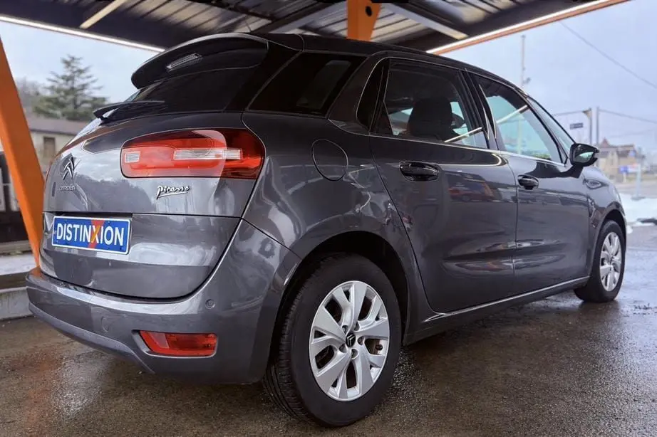 Vue 3/4 arrière droite d'une Citroën C4 Picasso gris platinium métallisé sous abri, avec jantes alliage et feux arrière allongés.