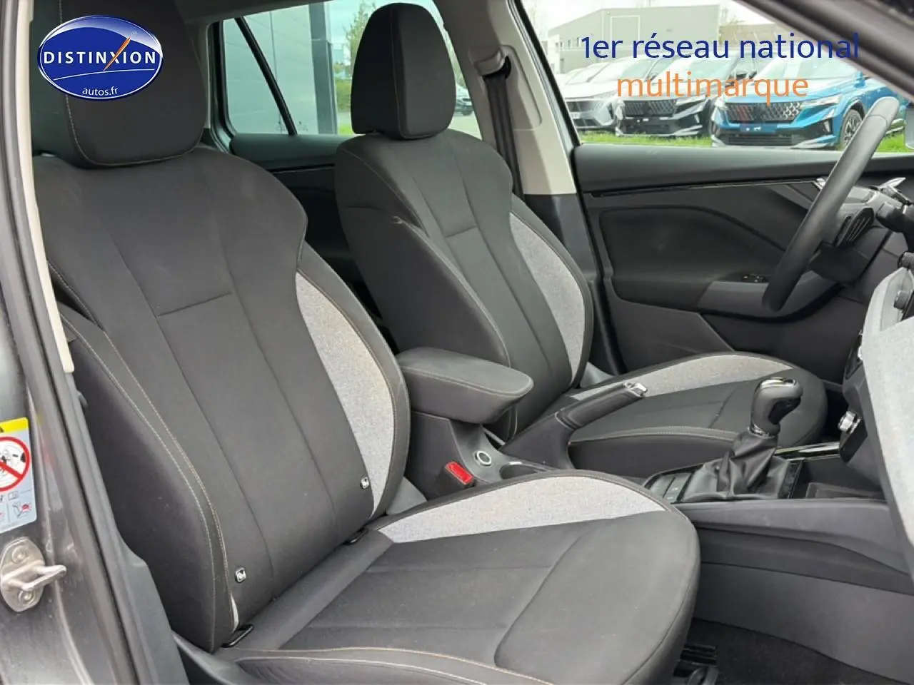 Vue intérieure côté avant gauche du Skoda Kamiq gris 2025, sièges tissu bicolore avec accoudoir central.