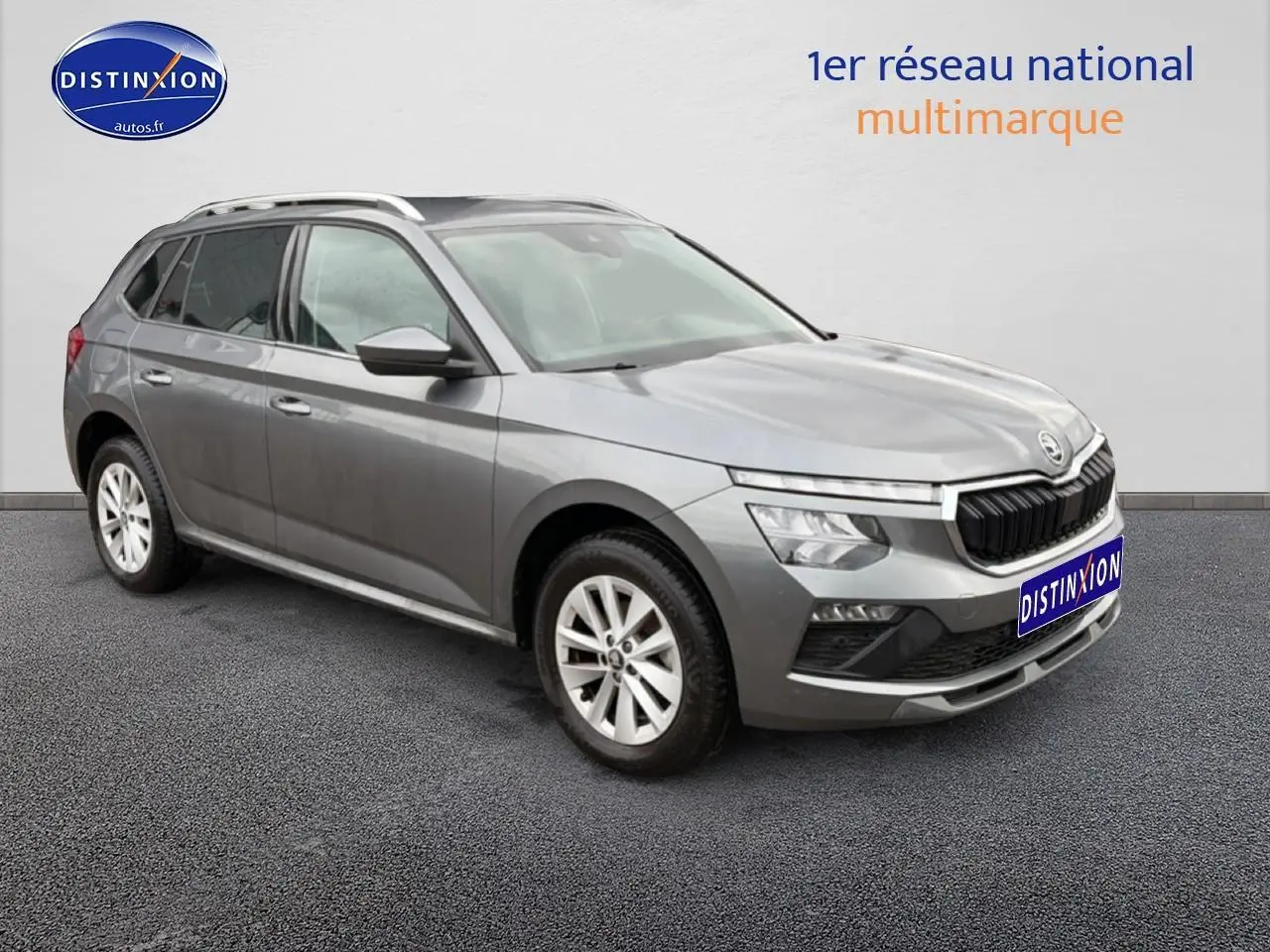 Vue 3/4 avant gauche d'un Skoda Kamiq gris avec calandre chromée et barres de toit visibles.