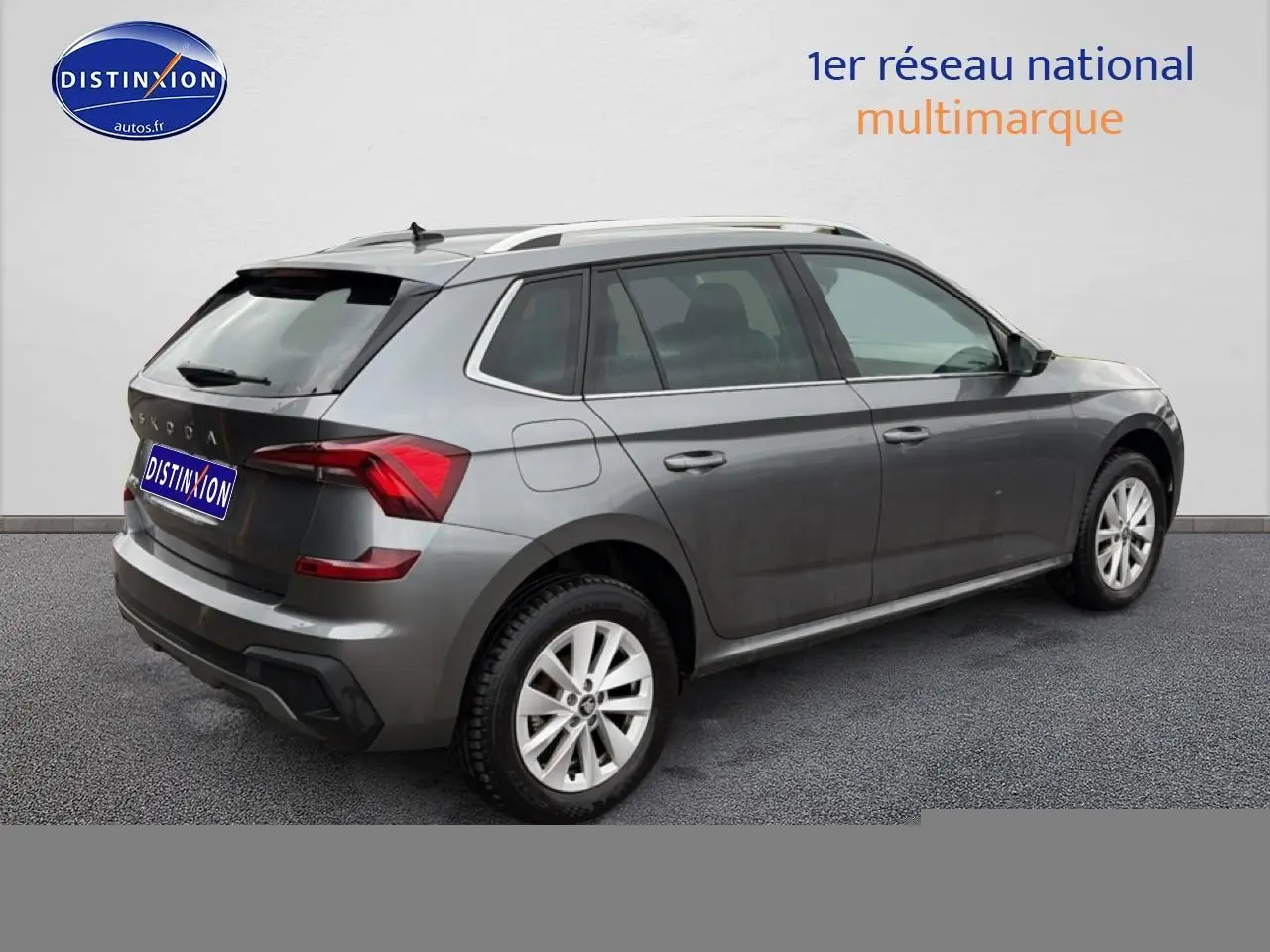 Vue 3/4 arrière droite d'un Skoda Kamiq gris 2025 avec barres de toit et jantes alu visibles.