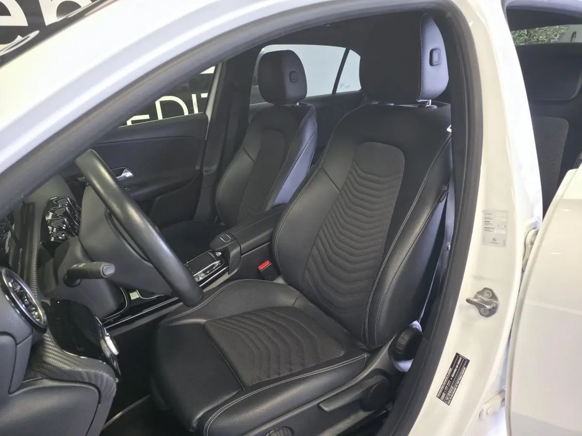 Vue intérieure côté conducteur d'une Mercedes Classe A blanche 2019, sièges sport noirs en tissu et similicuir.