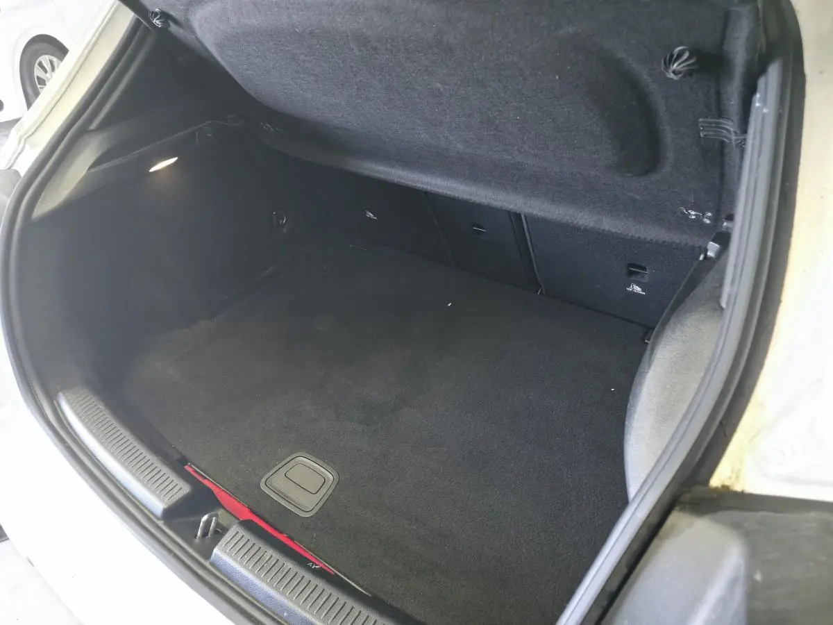 Coffre ouvert vu de dessus d'une Mercedes Classe A blanche, montrant la moquette noire et l'éclairage intérieur.