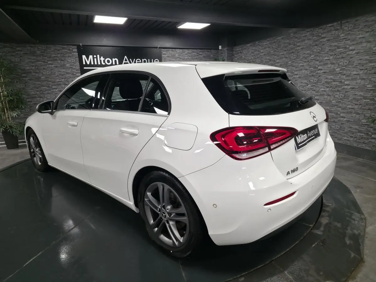 Vue 3/4 arrière droite d'une Mercedes Classe A 160 blanche avec jantes alliage gris Himalaya dans un showroom.