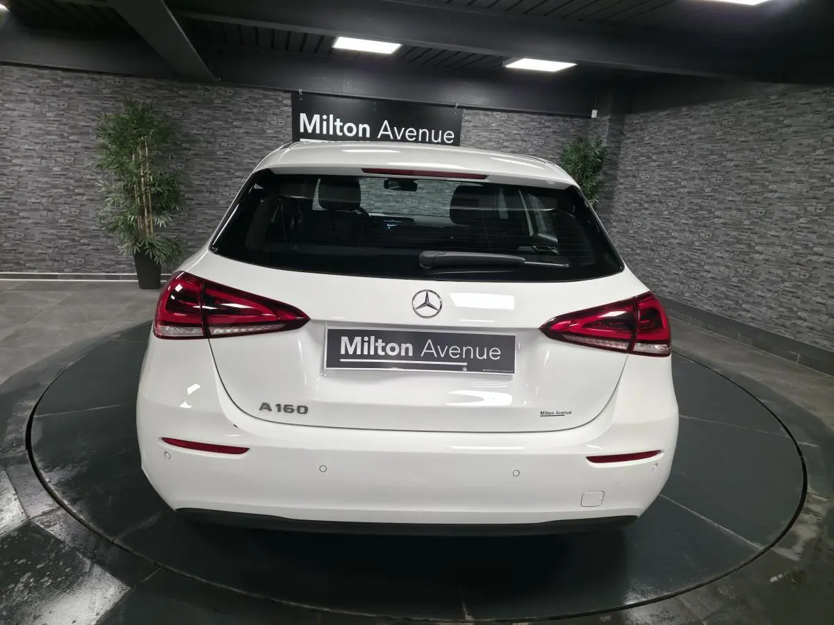 Vue arrière d'une Mercedes Classe A 160 blanche avec feux LED et logo Mercedes visible sur fond intérieur showroom.