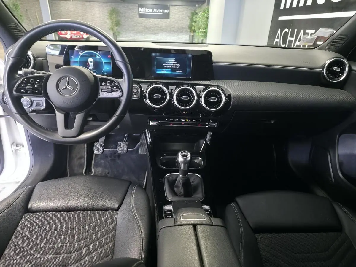 Vue intérieure avant de la Mercedes Classe A 160 Style Line 2019, volant cuir, tableau de bord numérique et levier de vitesse manuel.