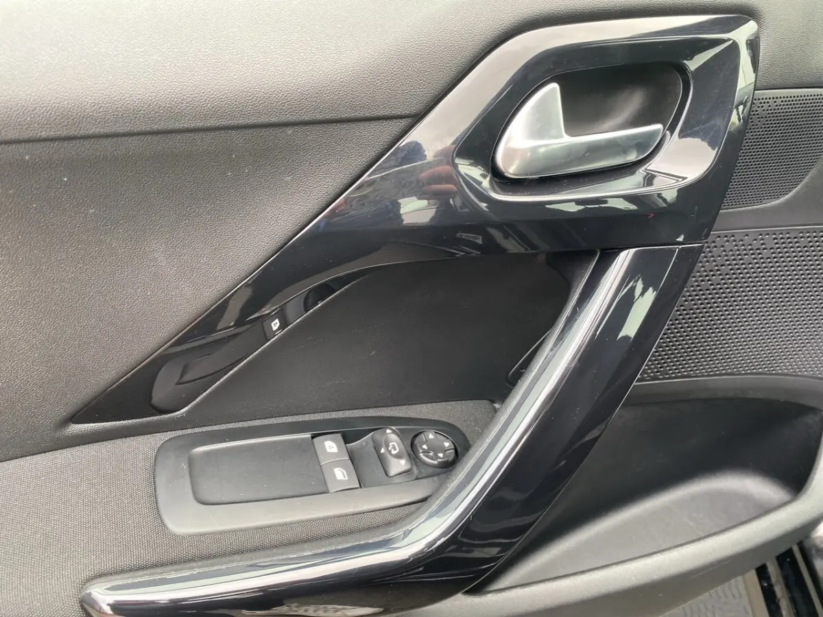 Vue rapprochée de la porte côté conducteur noire de la Peugeot 208 AFFAIRE avec commandes électriques des vitres et poignée brillante.